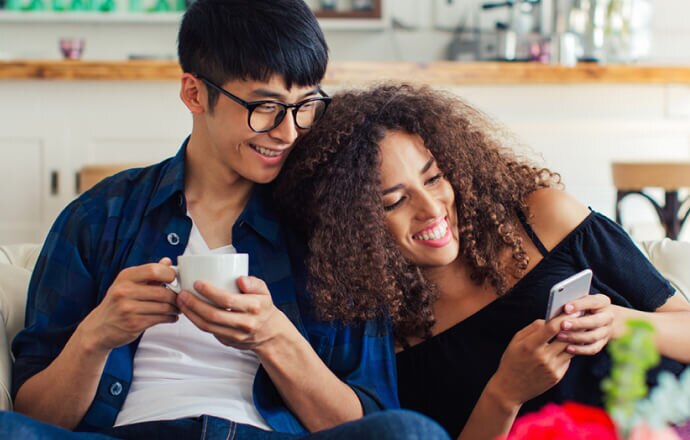 en mand og nogle kvinder sidder i en sofa og kigger på en mobiltelefon, der er beskyttet med Norton 360 for Mobile.