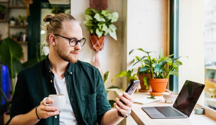 Mand, der drikker kaffe og har en mobiltelefon, der er beskyttet med Norton 360 for Mobile.