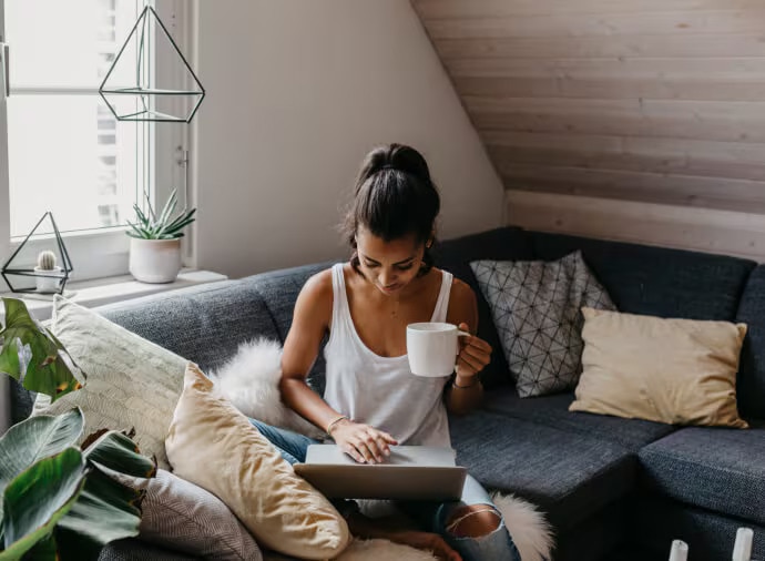 Kvinde sidder på en sofa med et krus og en laptop